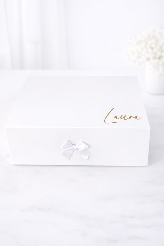 Weiße Geschenkbox mit Schleife und goldener Aufschrift „Laura“ auf hellem Hintergrund