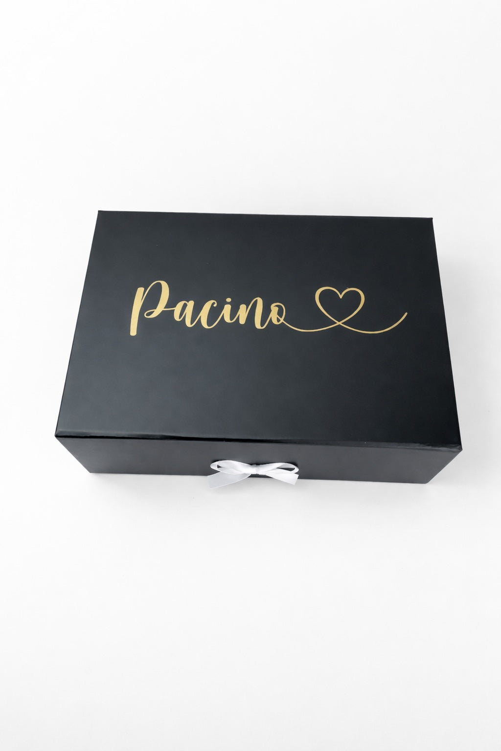 Schwarze Geschenkbox mit goldenem Schriftzug ‚Pacino‘ und Herz auf hellem, minimalistischem Hintergrund