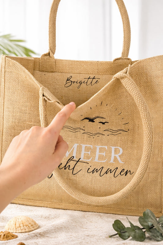 Personalisierte Jute Strandtasche mit Aufdruck „Meer geht immer“ und Name Brigitte im Inneren, Hand zeigt auf die Personalisierung der Beach Bag.
