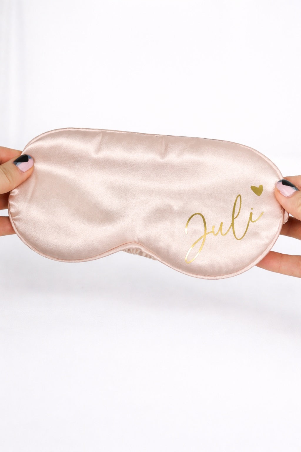 Personalisierte Schlafmaske aus Satin in Rosa mit Name ‚Juli‘ in Gold, gehalten vor hellem, minimalistischem Hintergrund