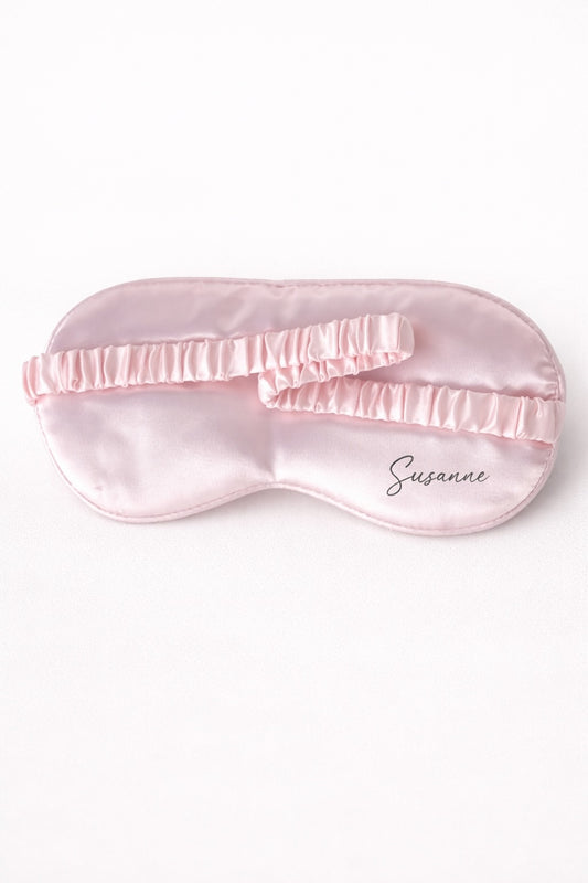 Personalisierte rosa Schlafmaske aus Satin mit Namen Susanne und elastischem Band auf hellem Hintergrund