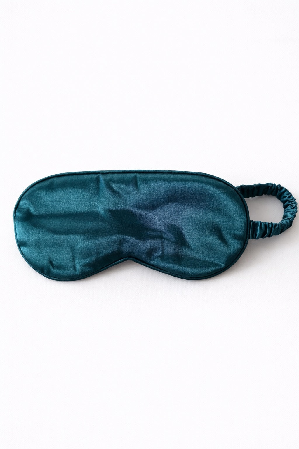 Dunkelgrüne Satin-Schlafmaske ohne Aufdruck auf hellem, minimalistischem Hintergrund