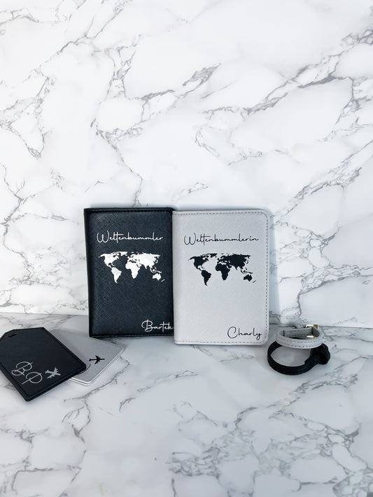 Personalisierte Reisepasshüllen in Schwarz und Weiß aus veganem Saffiano-Leder mit Weltkarten-Design und Namen, dazu passende Kofferanhänger mit Symbolen, dekorativ auf Marmor-Hintergrund arrangiert.