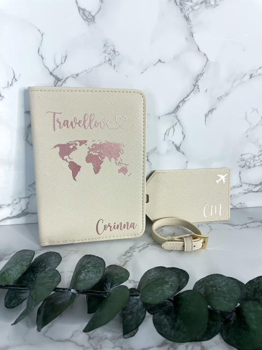 Personalisierte beige Reisepasshülle mit roségoldener Weltkarte und Schriftzug „Travellove“ sowie passendem Kofferanhänger mit Initialen und Flugzeugsymbol, dekorativ fotografiert auf Marmor-Hintergrund mit Eukalyptus.
