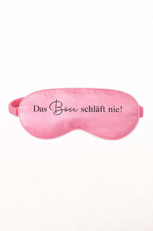 Coral Satin-Schlafmaske mit schwarzem Aufdruck „Das Böse schläft nie!“ auf hellem, neutralem Hintergrund