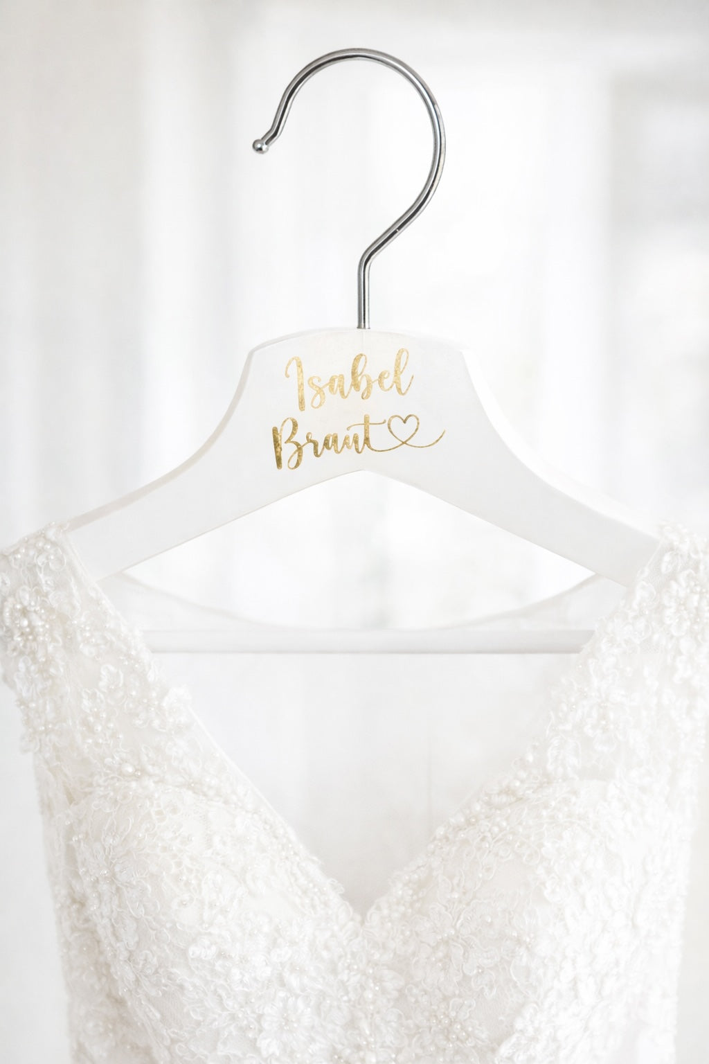 Personalisierter Brautbügel mit goldenen Aufkleber Name und Braut, daran hängt ein Brautkleid für Getting Ready Hochzeitsfotos.