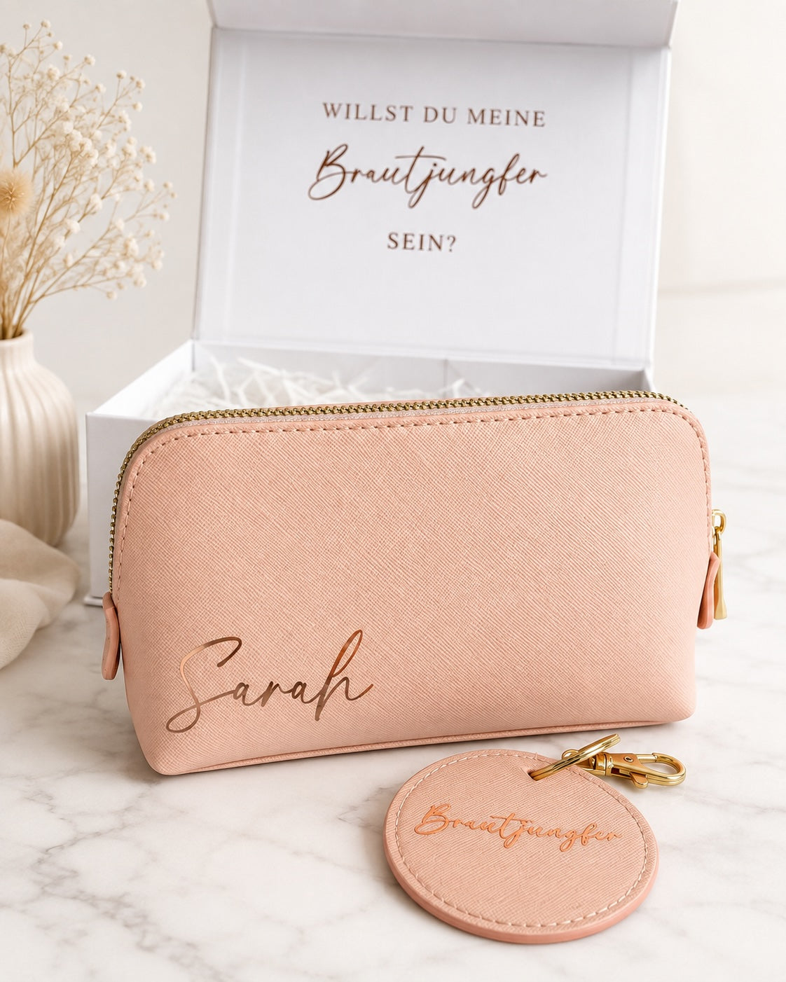 Personalisierte Brautjungfer Geschenkbox mit rosafarbener Kosmetiktasche mit Namen Sarah, rundem Brautjungfer-Anhänger und goldenen Details.