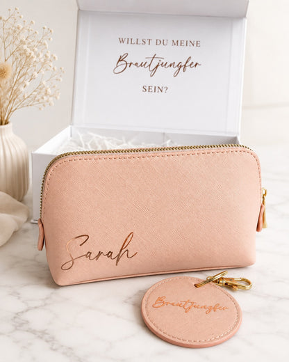 Personalisierte Brautjungfer Geschenkbox mit rosafarbener Kosmetiktasche mit Namen Sarah, rundem Brautjungfer-Anhänger und goldenen Details.