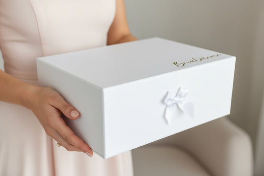 Weiße Geschenkbox für die Brautmama mit goldener Aufschrift „Brautmama“, stilvoll fotografiert .