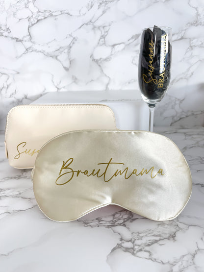 Elegante Schlafmaske mit goldener Aufschrift „Brautmama“, kombiniert mit personalisiertem Sektglas und Kosmetiktasche, arrangiert als hochwertiges Hochzeitsgeschenk.