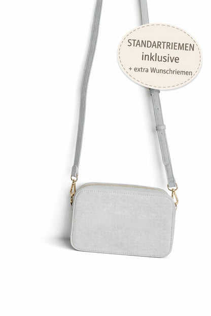 Graue Crossbody Tasche mit Standardriemen, inklusive zusätzlichem Wunschriemen zur Auswahl, auf hellem neutralem Hintergrund.