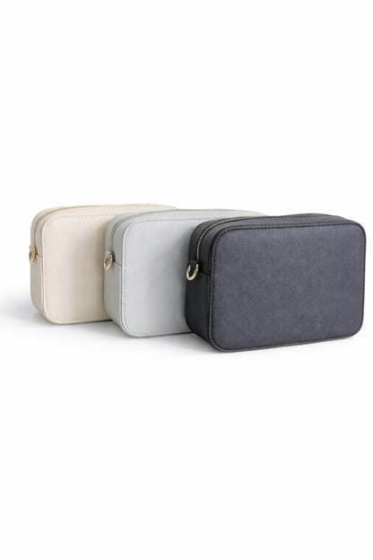 Drei Damen Crossbody Umhängetaschen in Creme, Grau und Schwarz auf hellem neutralem Hintergrund – minimalistische Tasche mit Reißverschluss und goldenen Details.