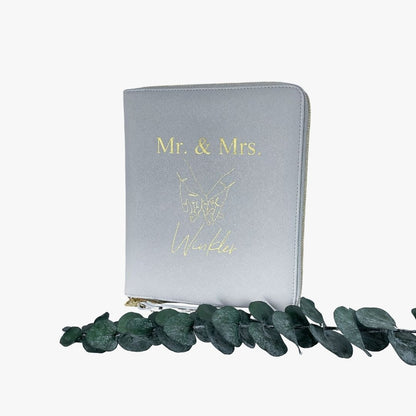 Personalisierter Dokumentenorganizer in Grau mit goldenem Aufdruck „Mrs. & Mrs.“ zur Aufbewahrung von Reiseunterlagen.