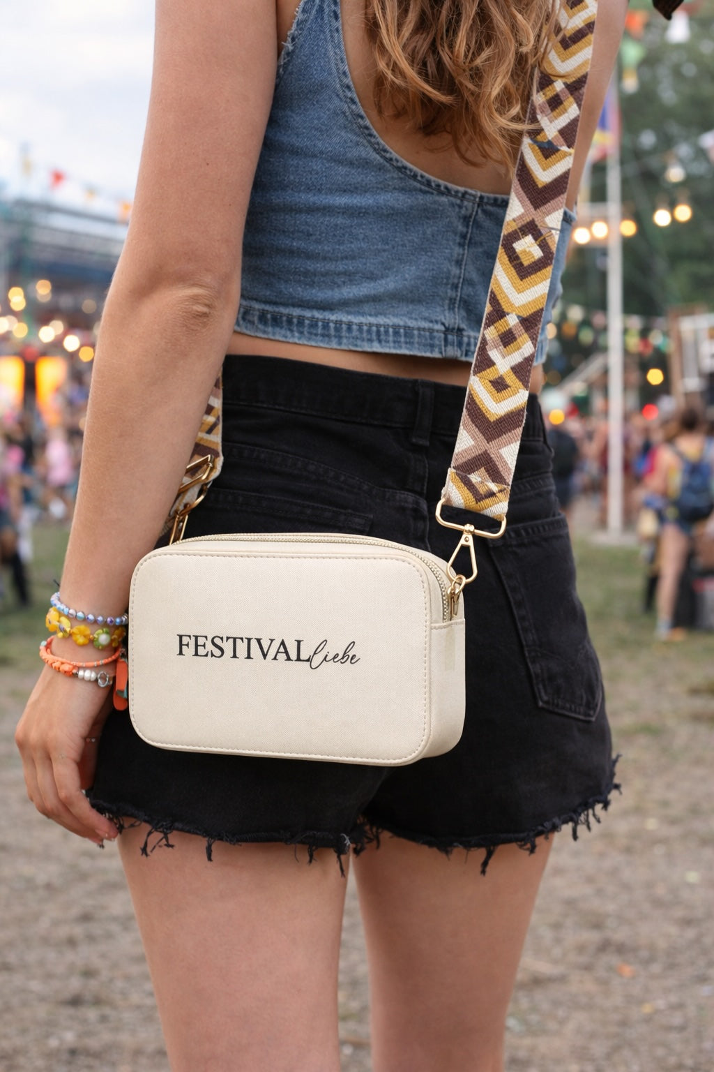 Frau trägt beige Crossbody Umhängetasche mit gemustertem Taschengurt auf einem Festival.