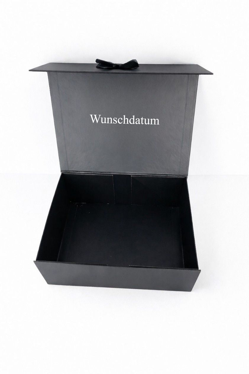 Geöffnete schwarze Geschenkbox für den Bräutigam mit personalisiertem Wunschdatum im Deckel auf hellem neutralen Hintergrund.