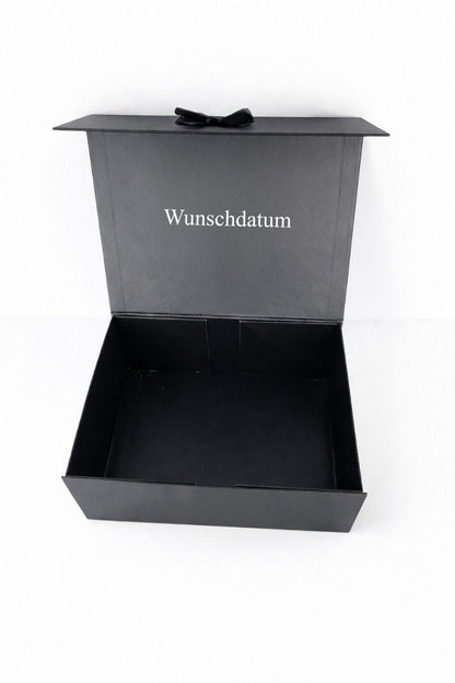Geöffnete schwarze Geschenkbox für den Bräutigam mit personalisiertem Wunschdatum im Deckel auf hellem neutralen Hintergrund.