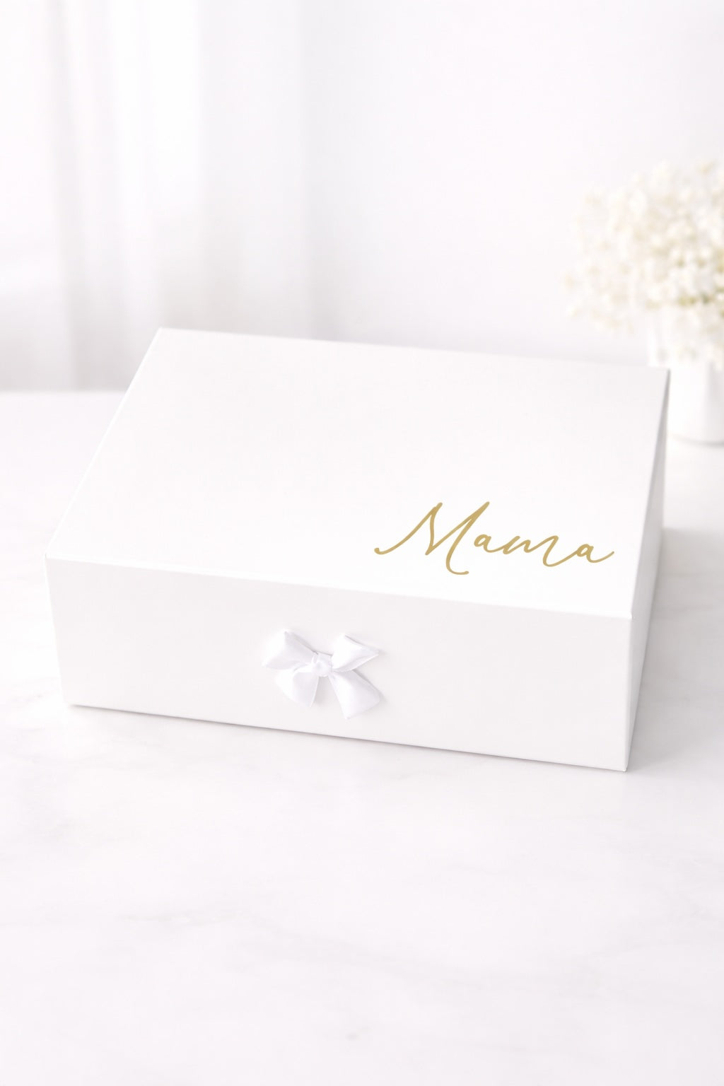 Weiße Geschenkbox mit goldener Aufschrift „Mama“ und Schleife auf hellem Hintergrund