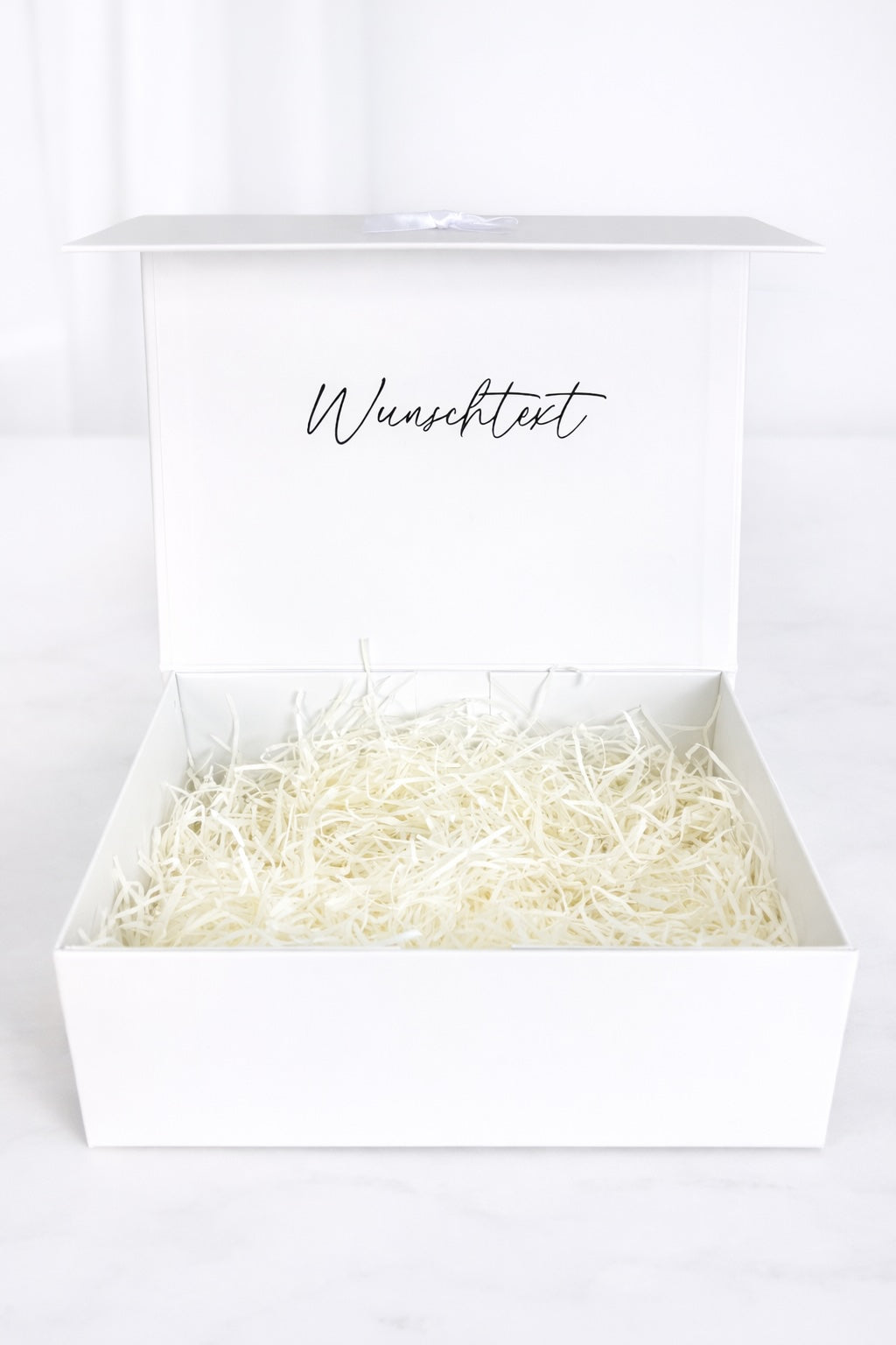 Offene weiße Geschenkbox mit Füllmaterial und Aufdruck „Wunschtext“ auf hellem Hintergrund