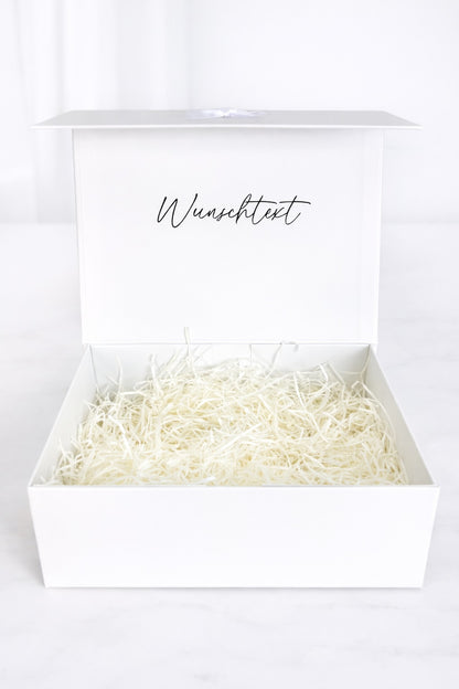 Offene weiße Geschenkbox mit Füllmaterial und Aufdruck „Wunschtext“ auf hellem Hintergrund