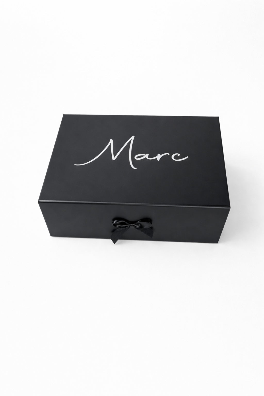 Schwarze, personalisierte Geschenkbox mit dem Namen Marc in weißer Schrift und schwarzer Schleife auf hellem, minimalistischem Hintergrund.“