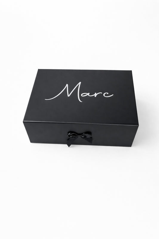 Schwarze, personalisierte Geschenkbox mit dem Namen Marc in weißer Schrift und schwarzer Schleife auf hellem, minimalistischem Hintergrund.“