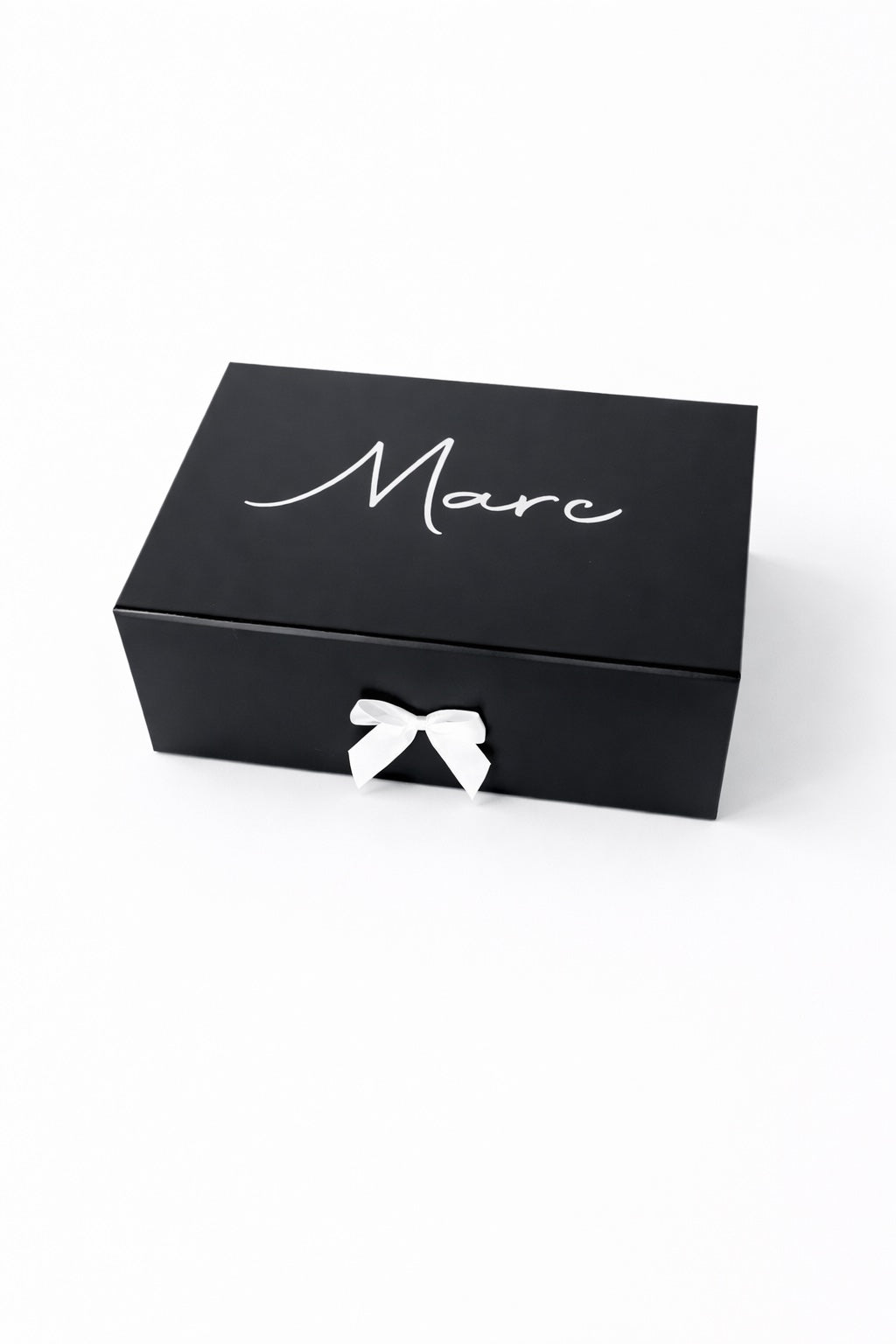 Schwarze, personalisierte Geschenkbox mit dem Namen Marc in weißer Schrift und weißer Schleife auf hellem, minimalistischem Hintergrund.