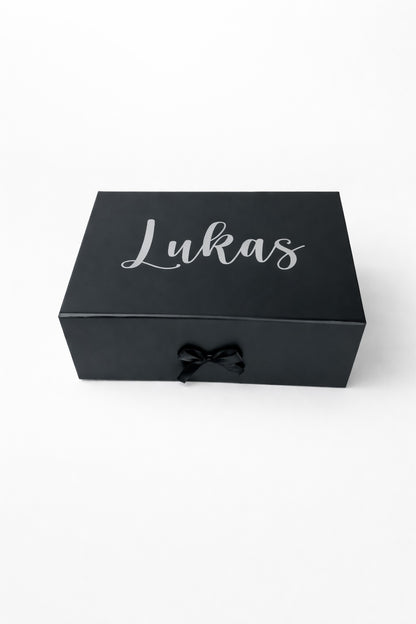 Schwarze, personalisierte Geschenkbox mit Name ‚Lukas‘ in silberner Schrift auf hellem, minimalistischem Hintergrund.“