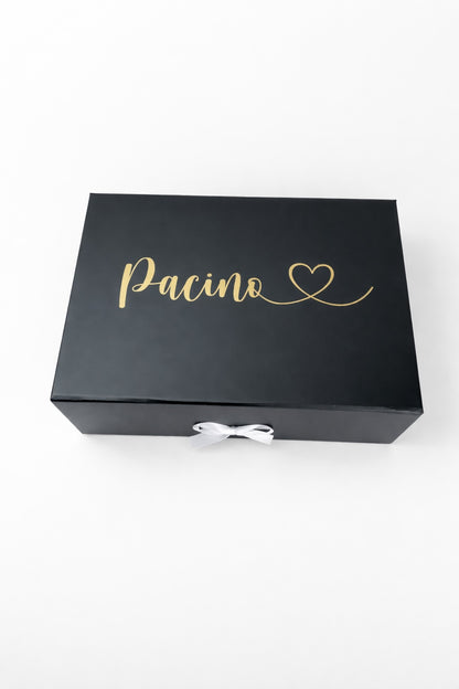 Schwarze Geschenkbox mit goldenem Schriftzug ‚Pacino‘ und Herz auf hellem, minimalistischem Hintergrund