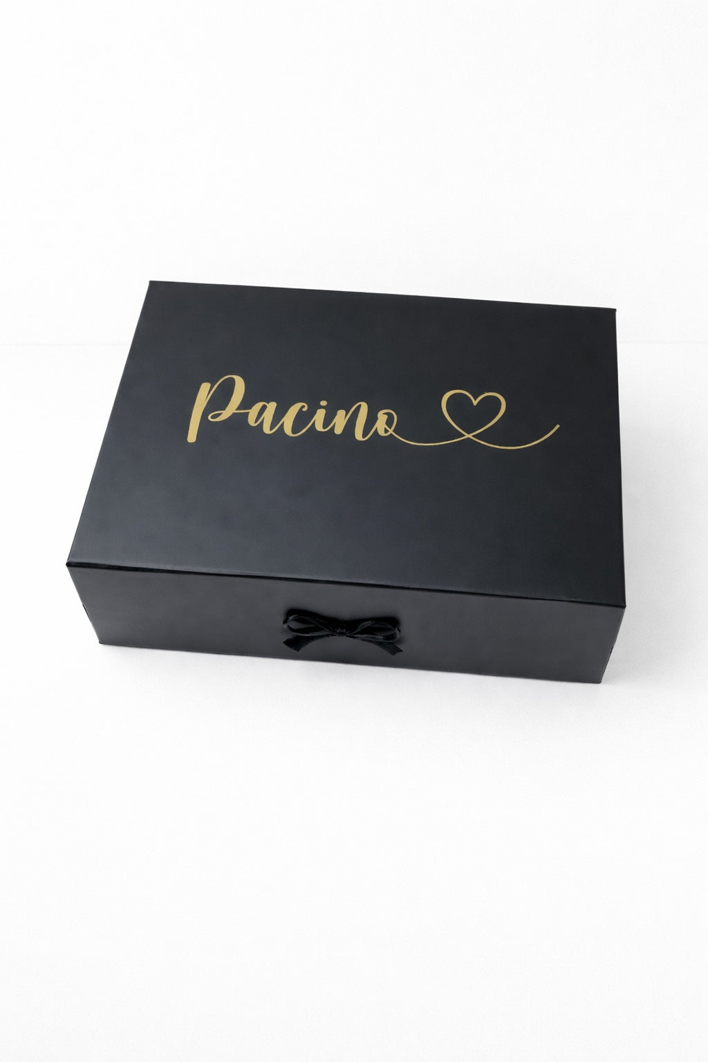 Schwarze Geschenkbox mit goldenem Schriftzug ‚Pacino‘ und Herz, mit schwarzer Schleife auf hellem, minimalistischem Hintergrund