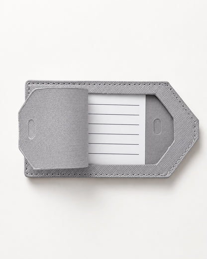 Hellgrauer Kofferanhänger mit sichtbarem Adress-Einleger auf hellem, neutralem Hintergrund in minimalistischer Produktaufnahme.