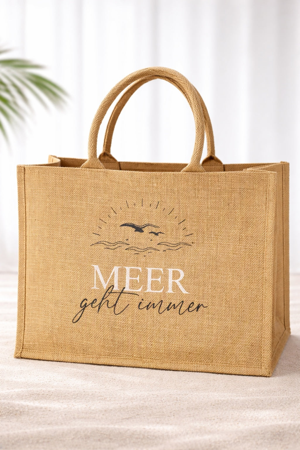 Natürliche Jute Strandtasche mit Aufdruck „Meer geht immer“, große Beach Bag aus Jute mit stabilen Griffen vor hellem neutralem Hintergrund.