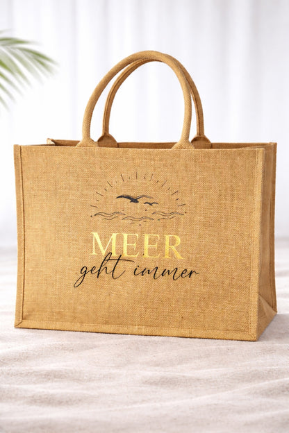 Jute Strandtasche mit Aufdruck „Meer geht immer“, Schriftzug MEER in Gold vor hellem neutralem Hintergrund, natürliche Beach Bag mit stabilen Griffen.