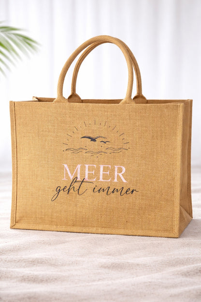 Jute Strandtasche mit Aufdruck „Meer geht immer“ in Roségold vor hellem neutralem Hintergrund, natürliche Beach Bag mit stabilen Griffen.