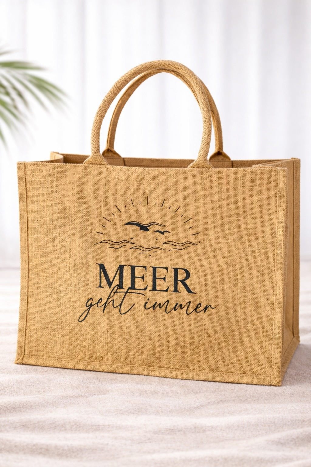Jute Strandtasche mit Aufdruck „Meer geht immer“ in schwarzer Schrift vor hellem neutralem Hintergrund, robuste Naturtasche mit stabilen Griffen im maritimen Design.