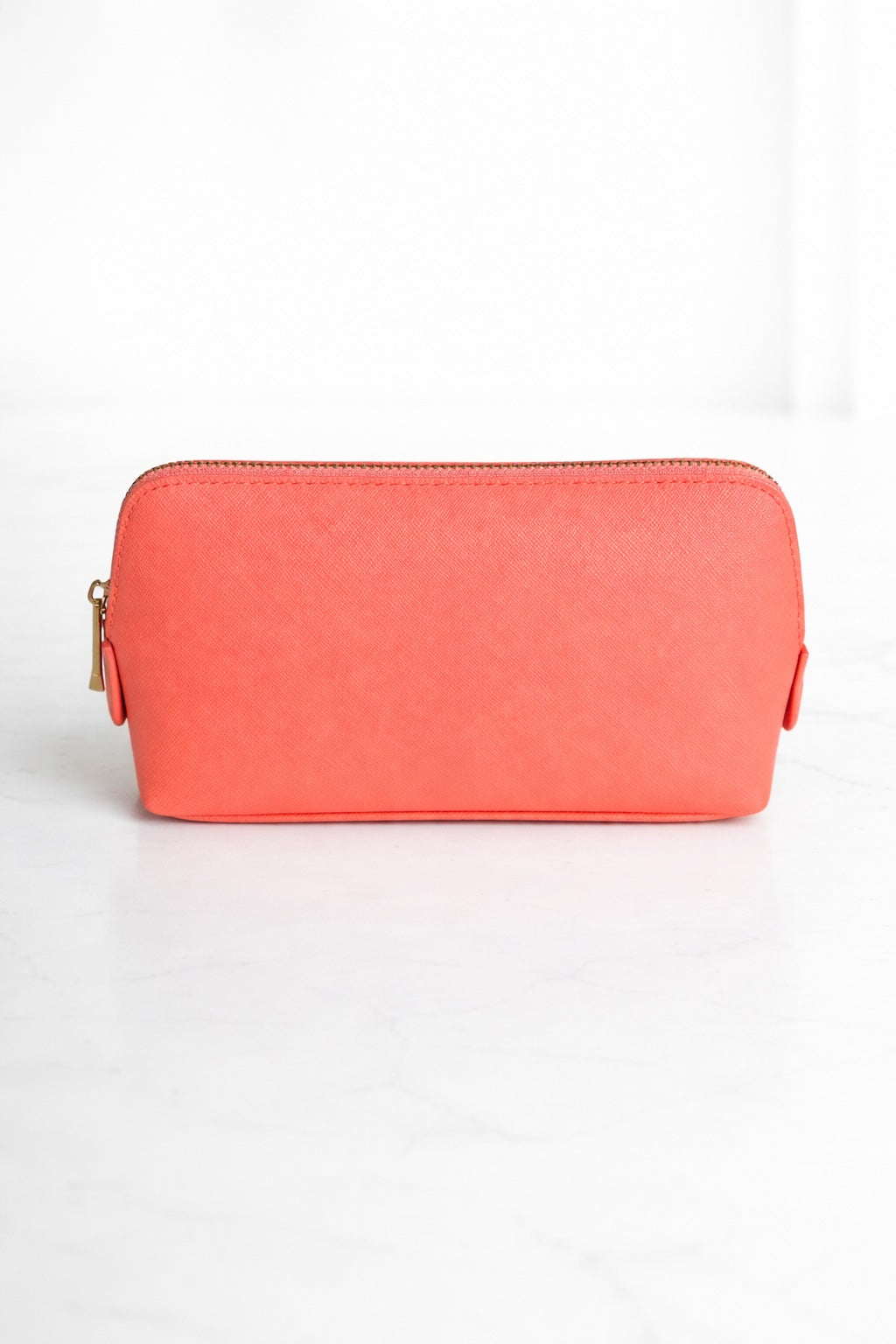 Coral Kosmetiktasche mit goldenem Reißverschluss auf hellem, neutralem Hintergrund