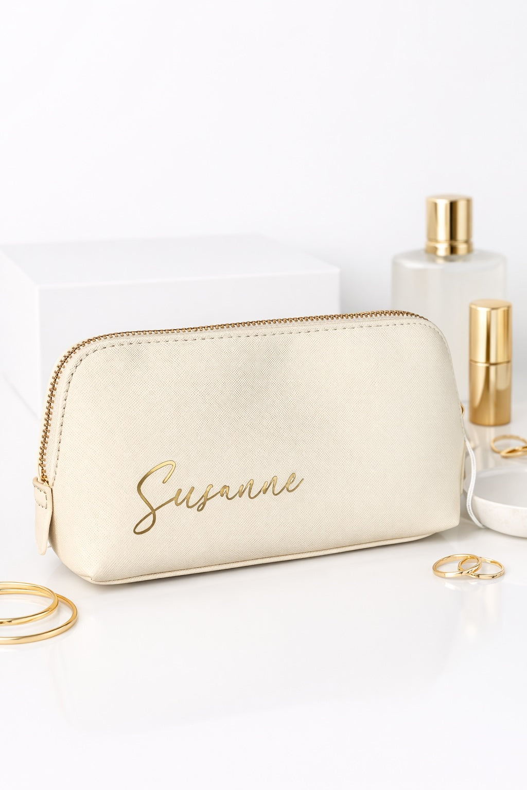 Personalisierte Kosmetiktasche in Creme mit goldener Aufschrift „Susanne“ auf hellem Hintergrund mit Beauty-Accessoires