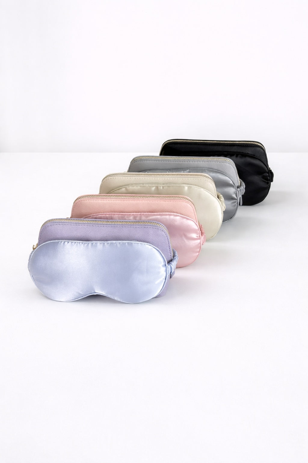 Übersicht verschiedener Kosmetiktaschen und Schlafmasken in mehreren Farben auf hellem, minimalistischem Hintergrund