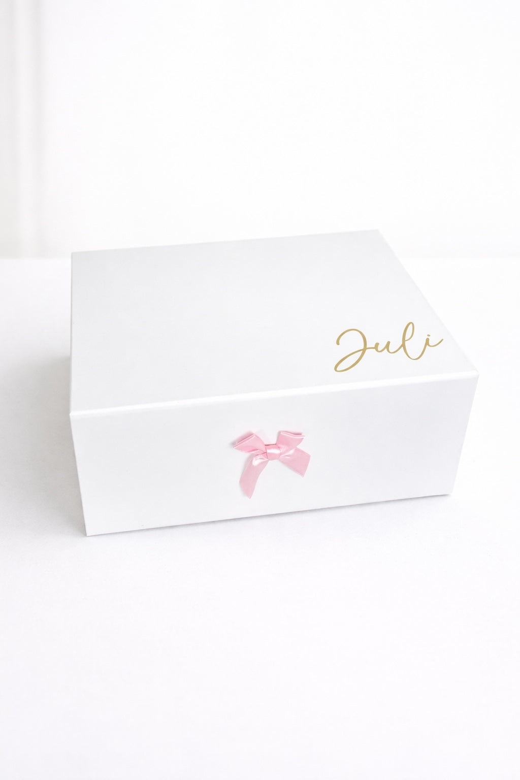 Weiße personalisierte Geschenkbox mit rosa Schleife und Name ‚Juli‘ in Gold auf hellem, minimalistischem Hintergrund