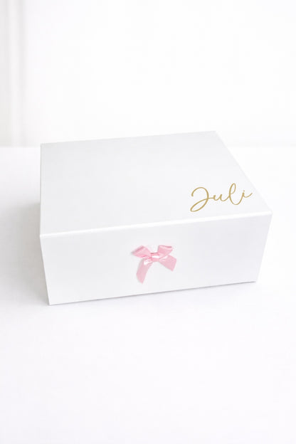 Weiße personalisierte Geschenkbox mit rosa Schleife und Name ‚Juli‘ in Gold auf hellem, minimalistischem Hintergrund