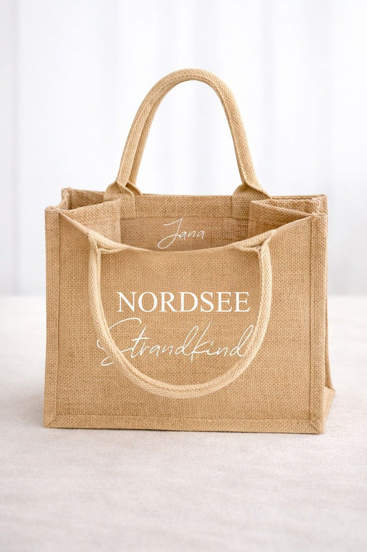 Personalisierte Jute Strandtasche „Nordsee Strandkind“ mit weißem Aufdruck und individuellem Namen im Innenbereich der Tasche vor hellem Hintergrund.