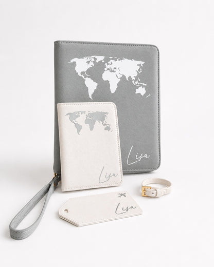 Personalisiertes Reiseaccessoires Set in Grau und Creme mit Weltkartenmotiv, Reiseorganizer, Reisepasshülle, Kofferanhänger und Armband auf hellem Hintergrund.