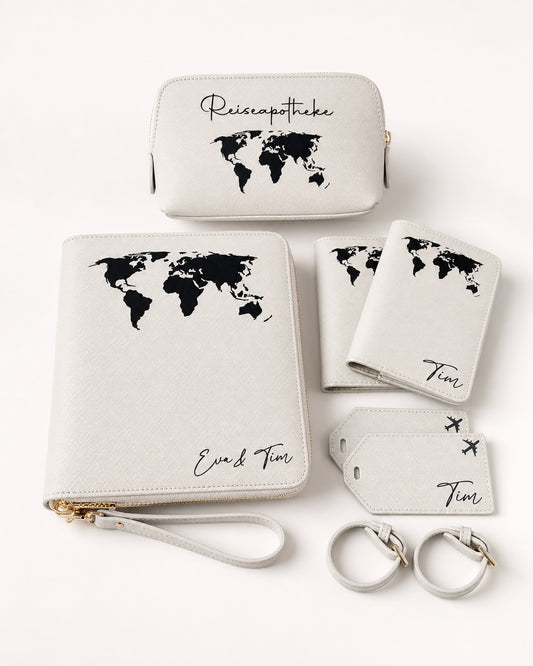 Personalisiertes Reiseset in Hellgrau mit schwarzem Weltkarten-Aufdruck, bestehend aus Reiseapotheke, Reiseorganizer, Reisepasshüllen und Kofferanhängern mit Namen Eva und Tim, minimalistisch auf hellem Hintergrund arrangiert.