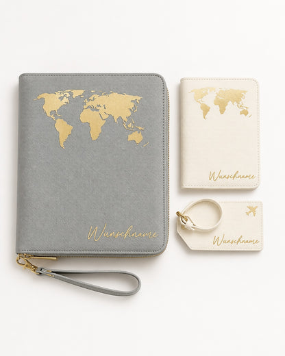 Flatlay eines personalisierten Reiseaccessoire-Sets mit grauem Reiseetui, cremefarbener Reisepasshülle und Kofferanhänger, jeweils mit goldener Weltkarten-Grafik und Namensaufdruck, sauber arrangiert auf hellem neutralem Hintergrund.