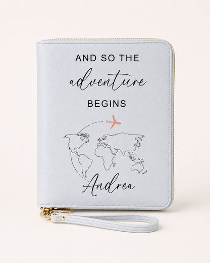 Weißer personalisierter Reiseorganizer mit der Aufschrift „And so the adventure begins“, Weltkarten-Motiv, Name „Andrea“ und Flugzeug in Roségold.