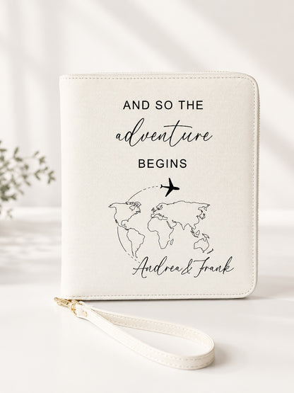 Beiger personalisierter Reiseorganizer mit schwarzem Schriftzug „And so the adventure begins“, Weltkarten-Motiv, Flugzeug und den Namen Andrea und Frank vor hellem, neutralem Hintergrund.