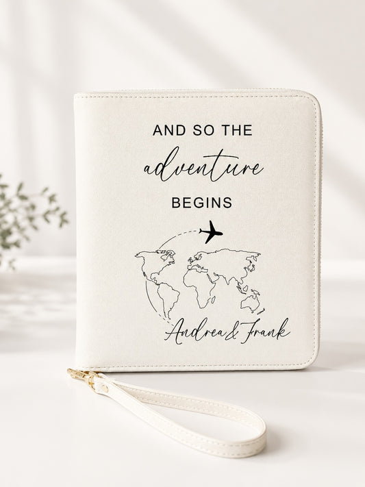 Beiger personalisierter Reiseorganizer mit schwarzem Schriftzug „And so the adventure begins“, Weltkarten-Motiv, Flugzeug und den Namen Andrea und Frank vor hellem, neutralem Hintergrund.