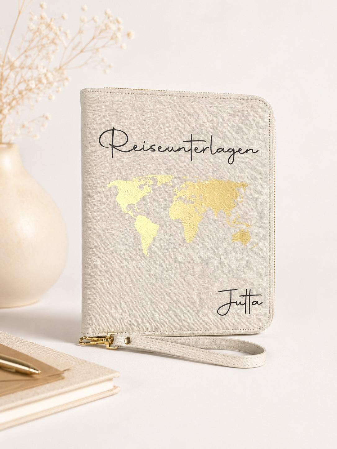 Beiger personalisierter Reiseorganizer mit goldenem Weltkarten-Motiv, schwarzem Schriftzug „Reiseunterlagen“ und dem Namen Jutta vor hellem, neutralem Hintergrund.