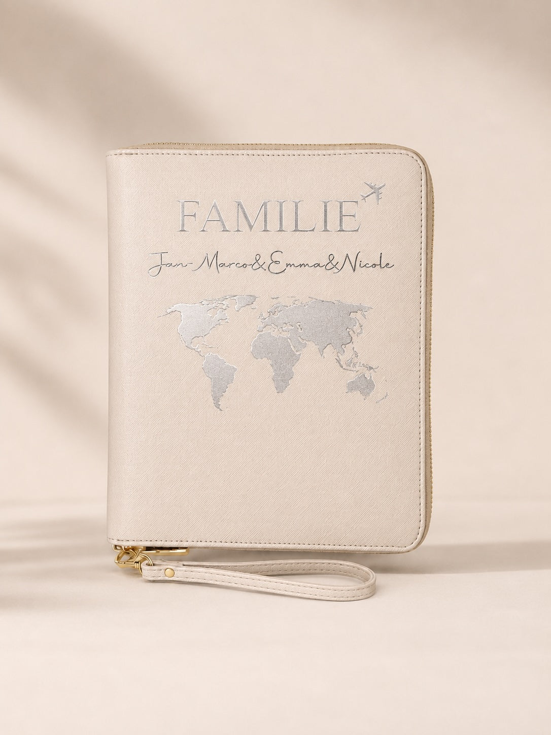 Beiger personalisierter Reiseorganizer für Familien mit silbernem Aufdruck, Weltkarte und Namen vor neutralem Hintergrund.