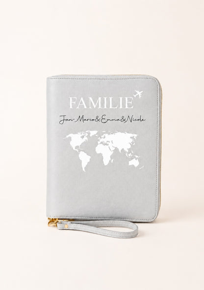 Personalisierter grauer Reiseorganizer mit Familienmotiv, Weltkarte und den Namen „Jan-Marcos, Emma & Nicole“ auf einem hellen, warmen Beigeton. Das Produkt steht im Mittelpunkt und wird vor einem schlichten, neutralen Hintergrund präsentiert.