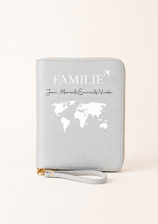 Personalisierter grauer Reiseorganizer mit Familienmotiv, Weltkarte und den Namen „Jan-Marcos, Emma & Nicole“ auf einem hellen, warmen Beigeton. Das Produkt steht im Mittelpunkt und wird vor einem schlichten, neutralen Hintergrund präsentiert.